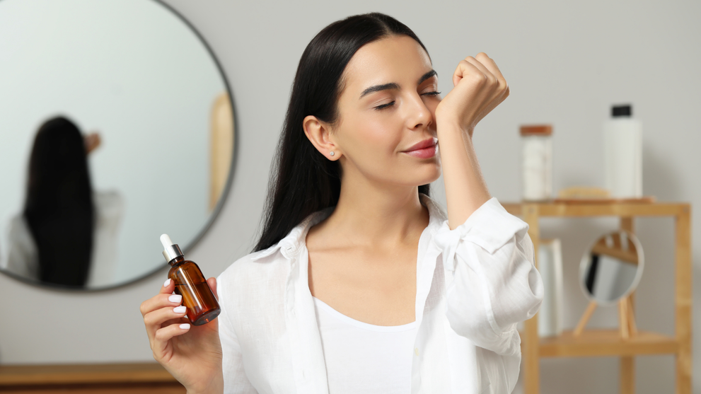 Woman smelling hair oil from a dropper bottle in bathroom